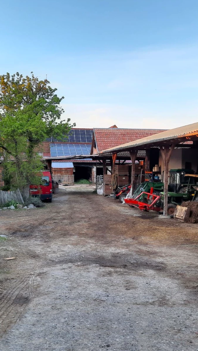 Solawi Hofplatz mit Photovoltaikanlage Hofplatz einer Solidarischen Landwirtschaft mit Scheune, auf deren Dach eine Solaranlage montiert ist, und abgestellten landwirtschaftlichen Geräten.